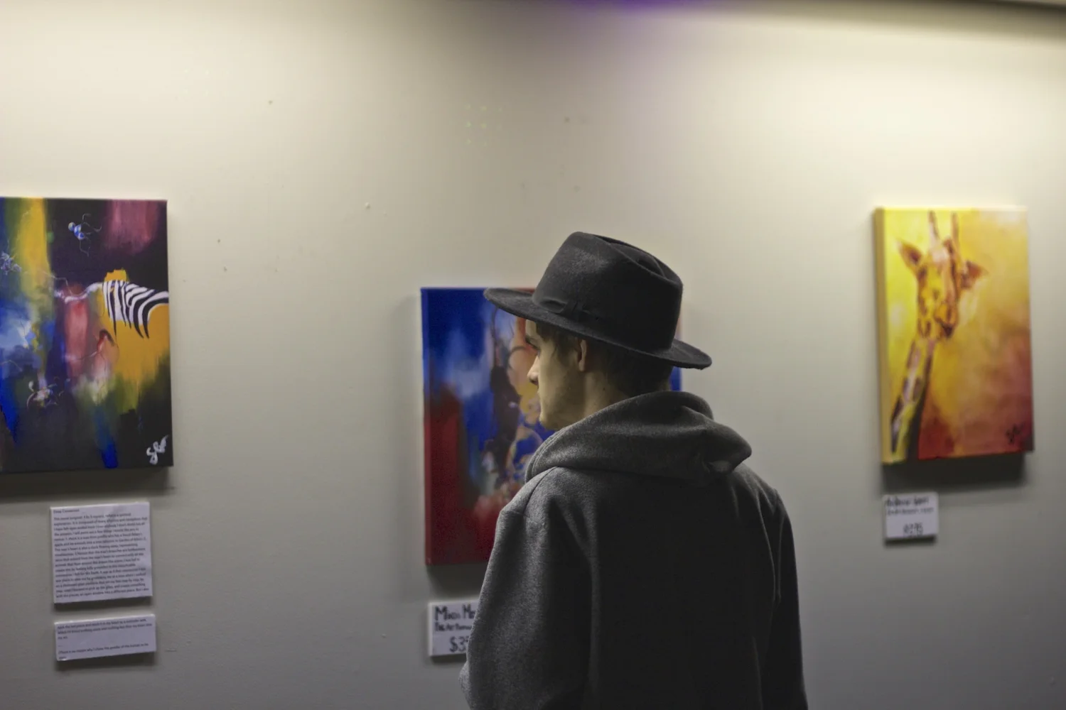 visitor in a hat viewing paintings on the wall
