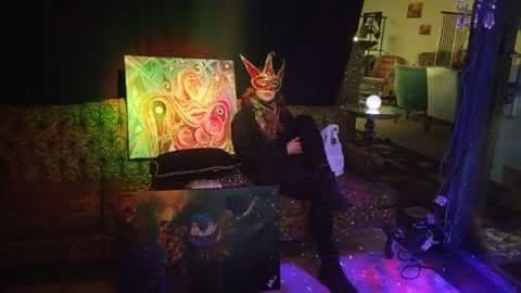 posing with a mask next to a painting under colored lights