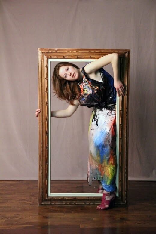 posing inside a large picture frame in a paint-covered dress